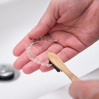 Patient using toothbrush to clean aligners in sink