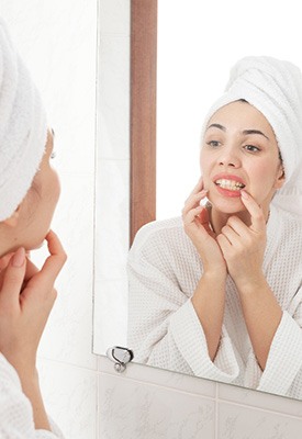 Woman in white robe looking at gums in reflection