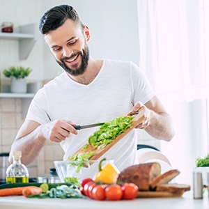Man smiling while preparing fruits and vegetables in kitchen