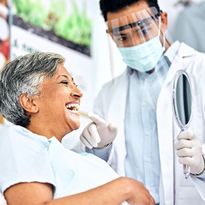 Woman smiling at reflection in small mirror with dentist