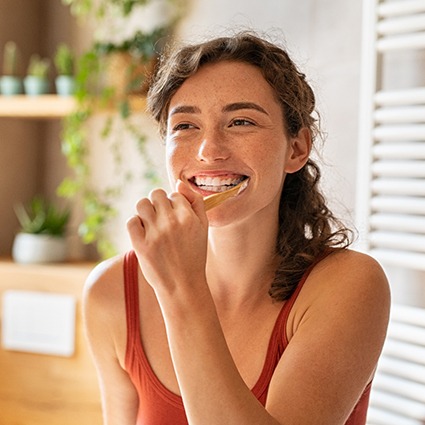 A woman brushing her teeth in front of a bathroom mirror