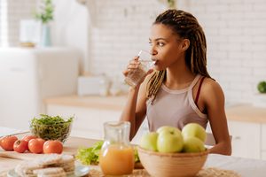Woman drinking water at kitchen counter with apples