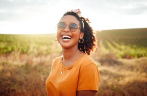 Woman smiling outdoors in a field under the sun.